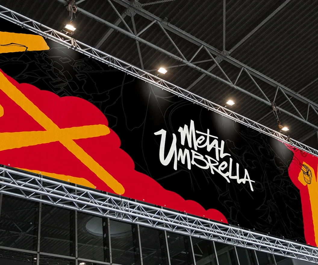 A long Metal Umbrella banner hung in a steel truss under a hall’s roof: the brush-lettered name in white on black, fine line drawings behind it, and red and yellow brushwork at both ends